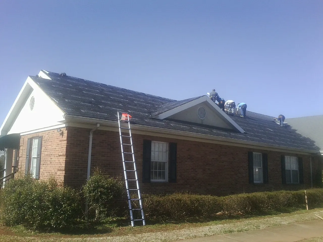 Crew tearing shingles off a brick ranch roof with a ladder set — Metal Roof Repair work by our crew in South Easton