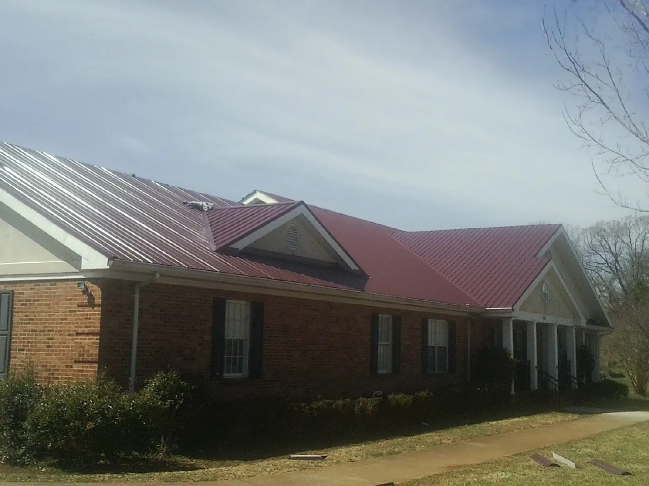 Red metal roof with gabled entries on a long brick building, from a Hail Damage Roof Repair job in South Easton