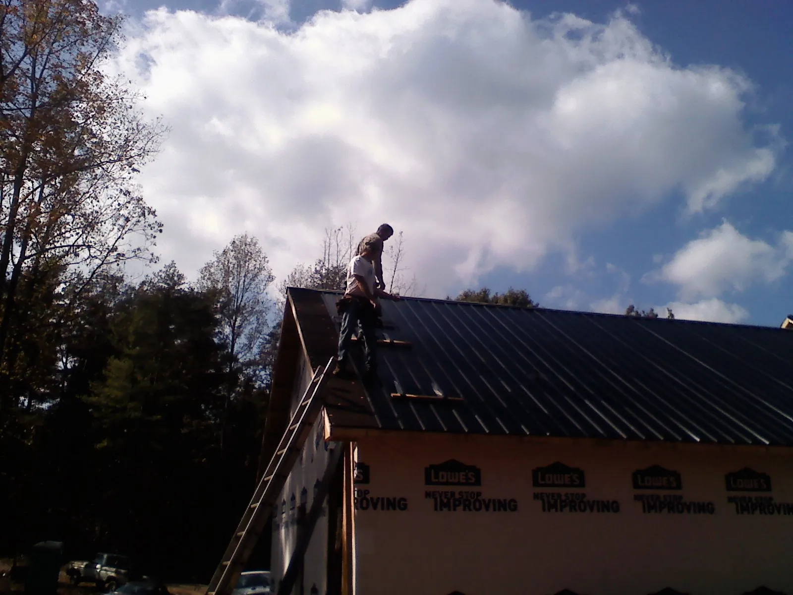 Roofer fastening dark metal panels high against a cloudy sky, from a Roof Inspection job in South Easton