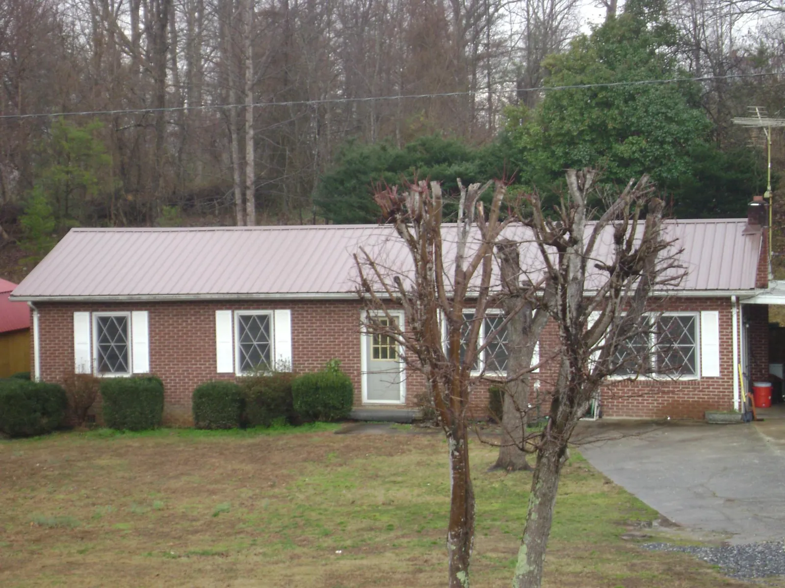Mauve metal roof on a brick ranch home behind bare trees in South Easton