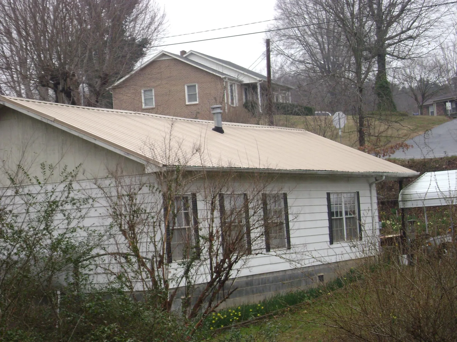 Tan metal roof on a white sided house set into a hillside — Commercial Roofing by Roofing Brothers in South Easton